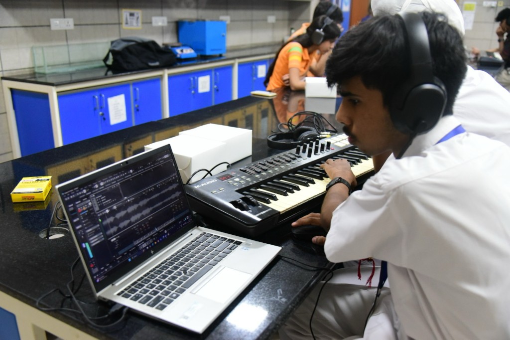 Student wearing headphones while working at a MIDI keyboard and laptop in the music production lab